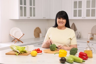 Beautiful overweight woman preparing healthy meal at table in kitchen