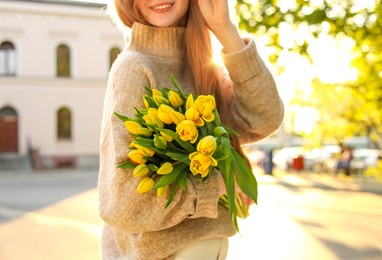 Teenage girl with bouquet of yellow tulips on city street, closeup