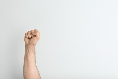 Young man showing clenched fist on light background. Space for text