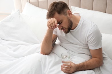Man with glass of water and pill suffering from migraine in bed