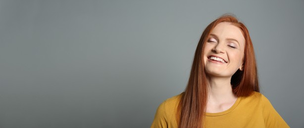 Candid portrait of happy young woman with charming smile and gorgeous red hair on grey background