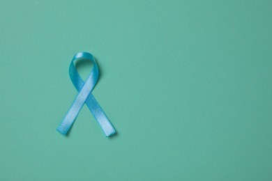 Photo of Light blue awareness ribbon on turquoise background, top view. Space for text
