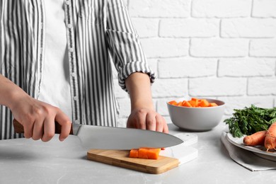 Woman cutting fresh ripe juicy carrots at light grey table, closeup