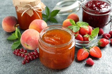 Jars with different jams and fresh fruits on grey table, closeup