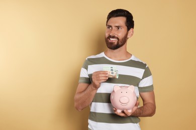 Happy man putting money into piggy bank on beige background, space for text