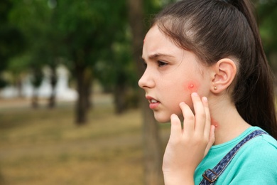 Girl touching cheek with insect bite in park. Space for text