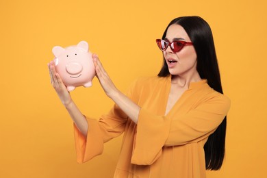 Photo of Emotional young woman with piggy bank on orange background