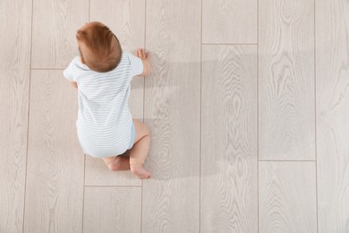 Photo of Cute baby crawling on floor, top view. Space for text