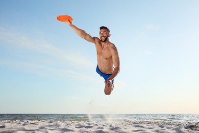 Sportive man jumping and catching flying disk at beach