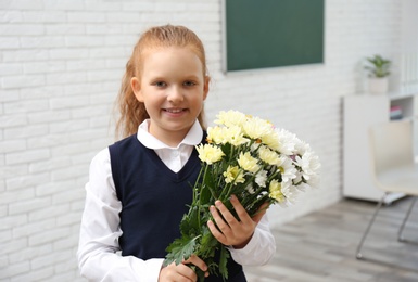 Happy schoolgirl with bouquet in classroom. Teacher's day