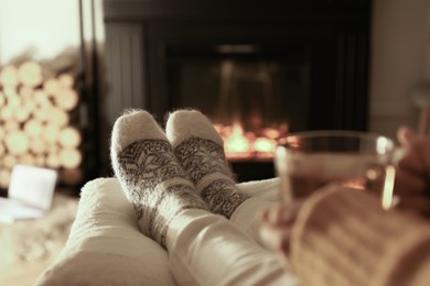 Photo of Woman in knitted socks resting near fireplace at home, closeup