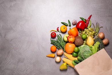 Paper bag with assortment of fresh organic fruits and vegetables on grey table, flat lay. Space for text