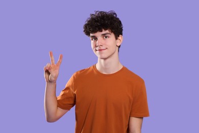Photo of Portrait of cute teenage boy showing peace gesture on violet background