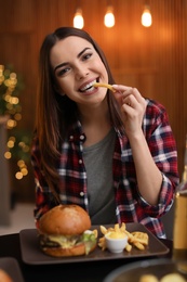 Photo of Young woman eating french fries and tasty burger in cafe