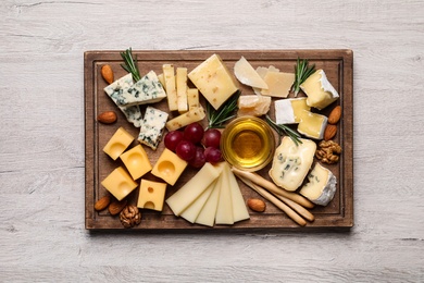 Cheese plate with honey, grapes and nuts on white table, flat lay