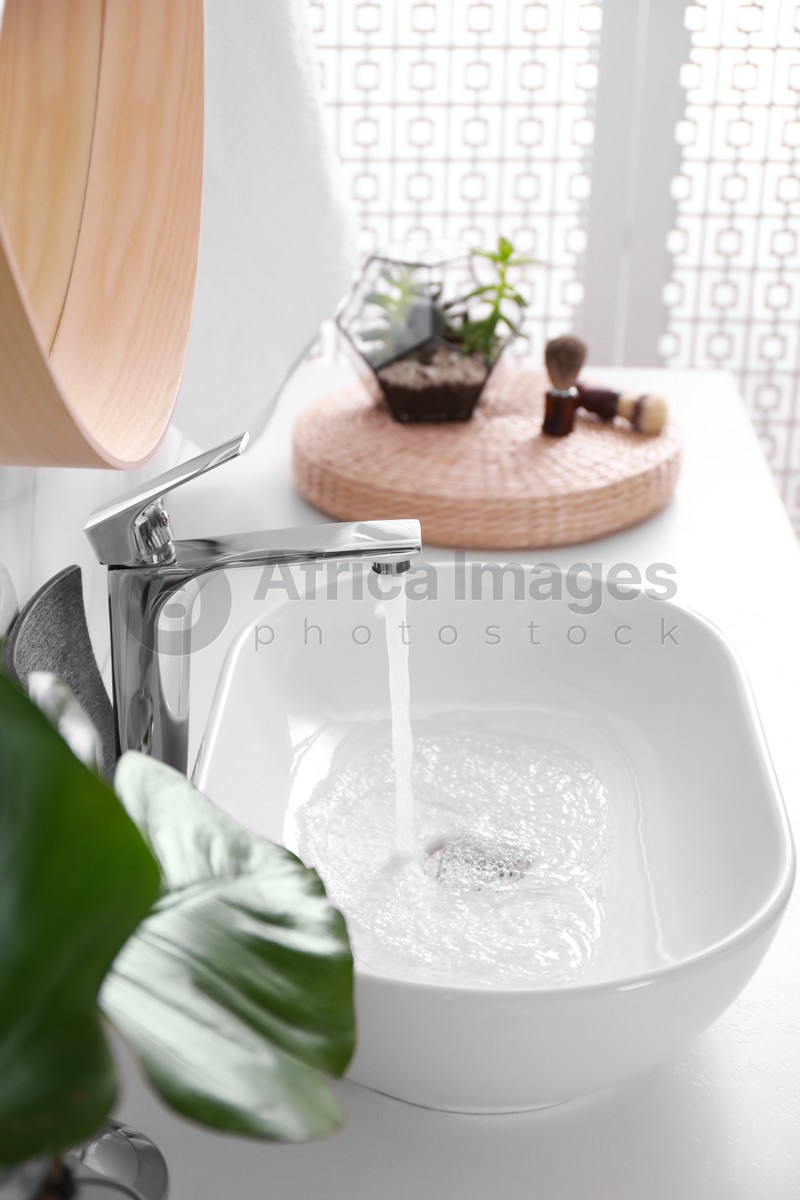 Sink with running water in stylish bathroom interior