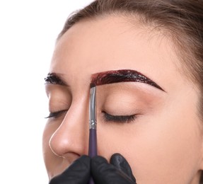 Beautician applying tint during eyebrows correction procedure on white background, closeup