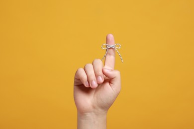 Man showing index finger with tied bow as reminder on orange background, closeup