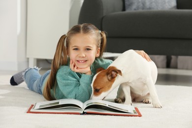 Photo of Cute girl reading book on floor with her dog at home. Adorable pet