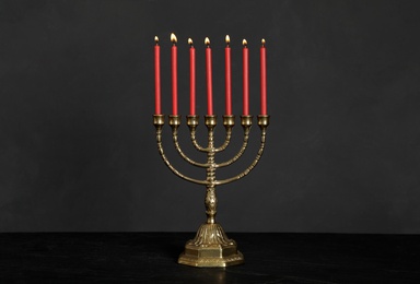 Golden menorah with burning candles on table against black background