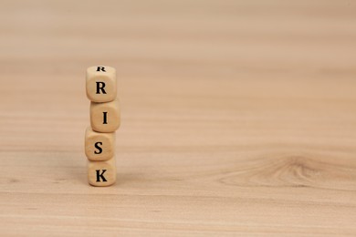 Stack of cubes with word Risk on wooden table. Space for text