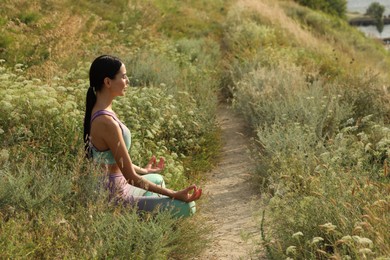 Photo of Young woman meditating on hill. Space for text
