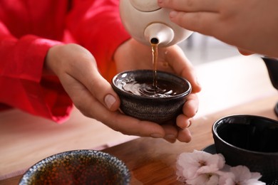Master pouring freshly brewed tea into guest's cup during traditional ceremony at table, closeup