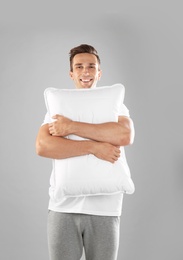 Young man in pajamas embracing pillow on gray background
