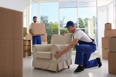 Moving service employees with armchair and cardboard boxes in room