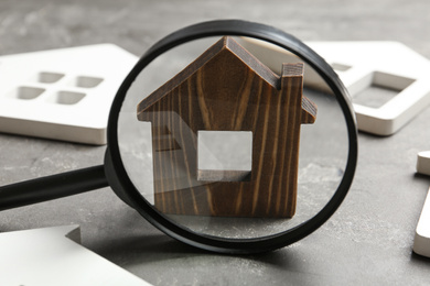 Magnifying glass and house models on grey stone table. Search concept