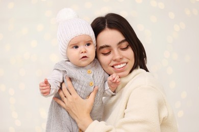 Happy young mother with her cute baby against blurred festive lights. Winter holiday