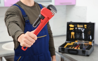 Male plumber holding pipe wrench in kitchen, closeup with space for text. Repair service