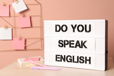 Stand with question Do You Speak English and stationery on table near pink wall