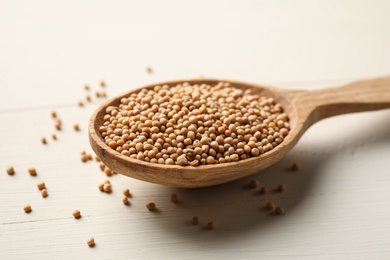 Mustard seeds with wooden spoon on white table, closeup