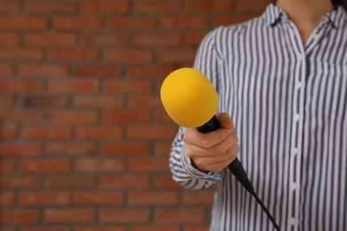 Journalist with microphone near brick wall, closeup. Space for text