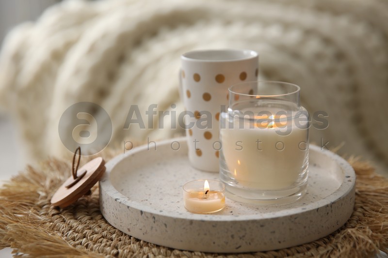 Cup of drink and burning candles on wicker mat indoors. Interior elements