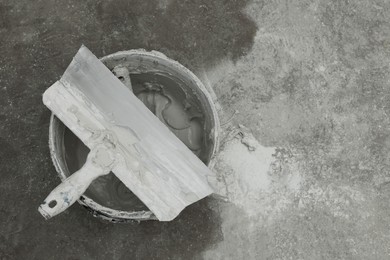 Bucket with plaster and putty knife on concrete floor, top view. Space for text