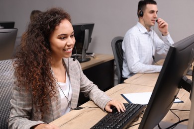 African American call center operator with headset and her colleague working in modern office