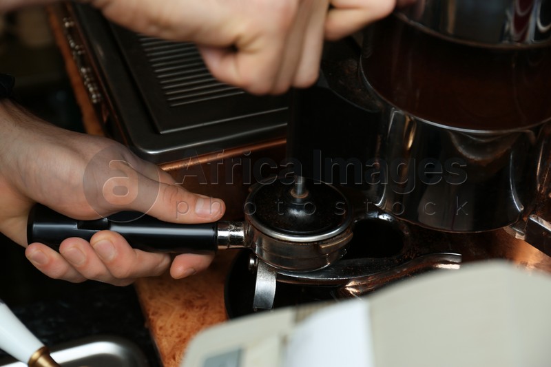 Barista pressing ground coffee with tamper in portafilter, closeup