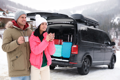Happy couple with drinks near car on snowy road. Winter vacation