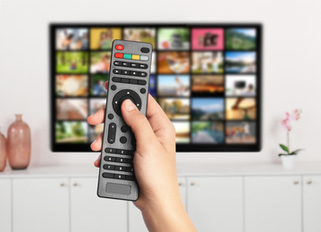 Image of Streaming video services. Woman using remote control to change channels on TV, closeup