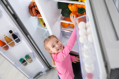 Little girl taking bell pepper out if refrigerator indoors, above view