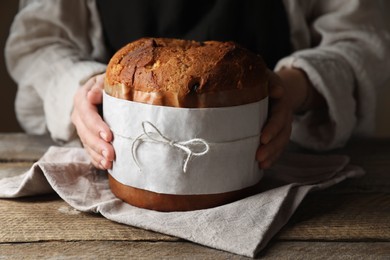 Photo of Woman holding delicious Panettone cake at wooden table, closeup. Traditional Italian pastry