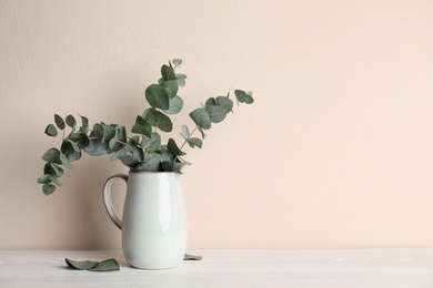 Vase with beautiful eucalyptus branches on white wooden table near beige wall. Space for text