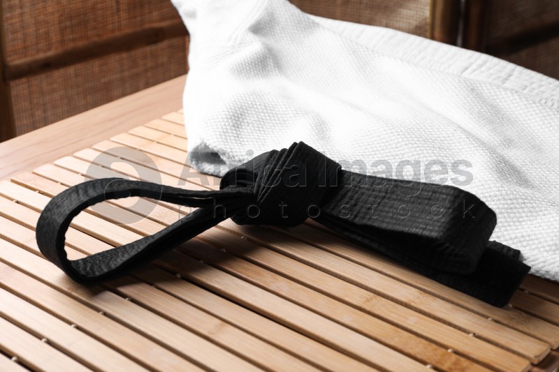 Photo of Martial arts uniform with black belt on table indoors