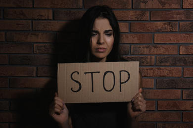 Abused young woman with sign STOP near brick wall. Domestic violence concept
