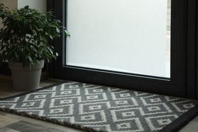 New clean door mat with pattern and beautiful houseplant on floor near entrance