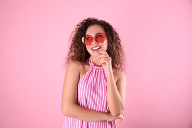 Young beautiful African-American woman wearing heart shaped glasses on pink background