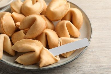 Photo of Tasty fortune cookies and paper with prediction on wooden table, closeup. Space for text