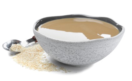 Tasty sesame paste in bowl, spoon and seeds on white background